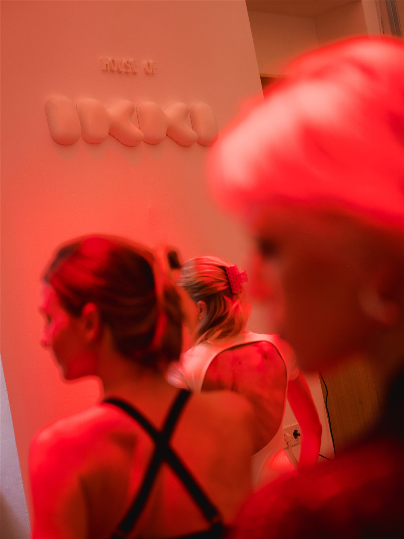 Members moving through the studio under red light, with the House of IKKI wordmark on the wall
