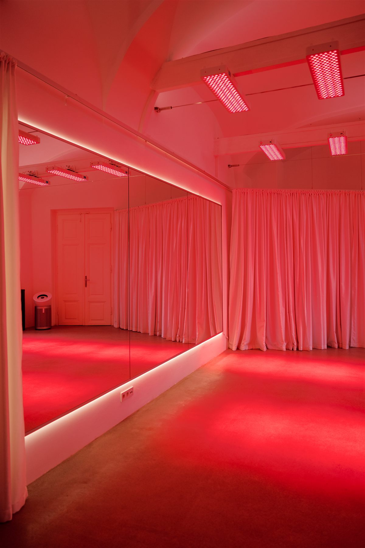 The studio room bathed in red light, with red light panels on the ceiling and a mirrored wall